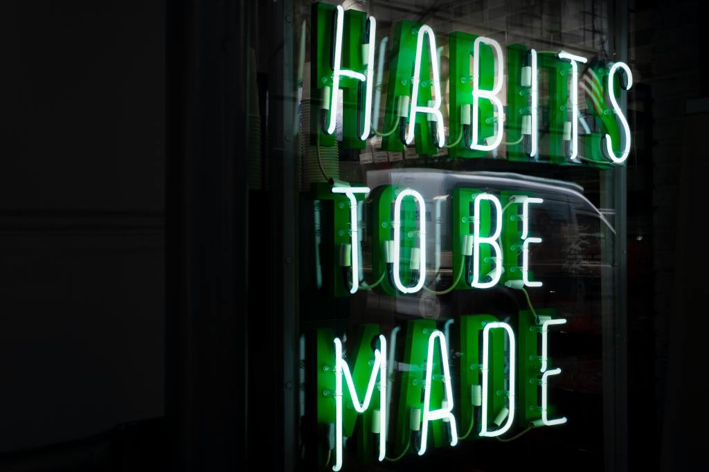 A green neon sign reading 'Habits To Be  Made'.